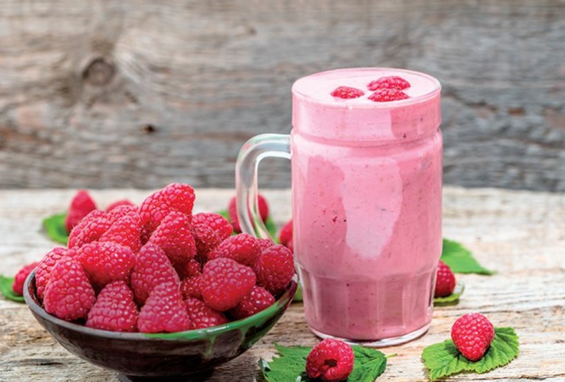 himbeer-shake in einem glas auf einem holztisch mit einer schale frischer himbeeren